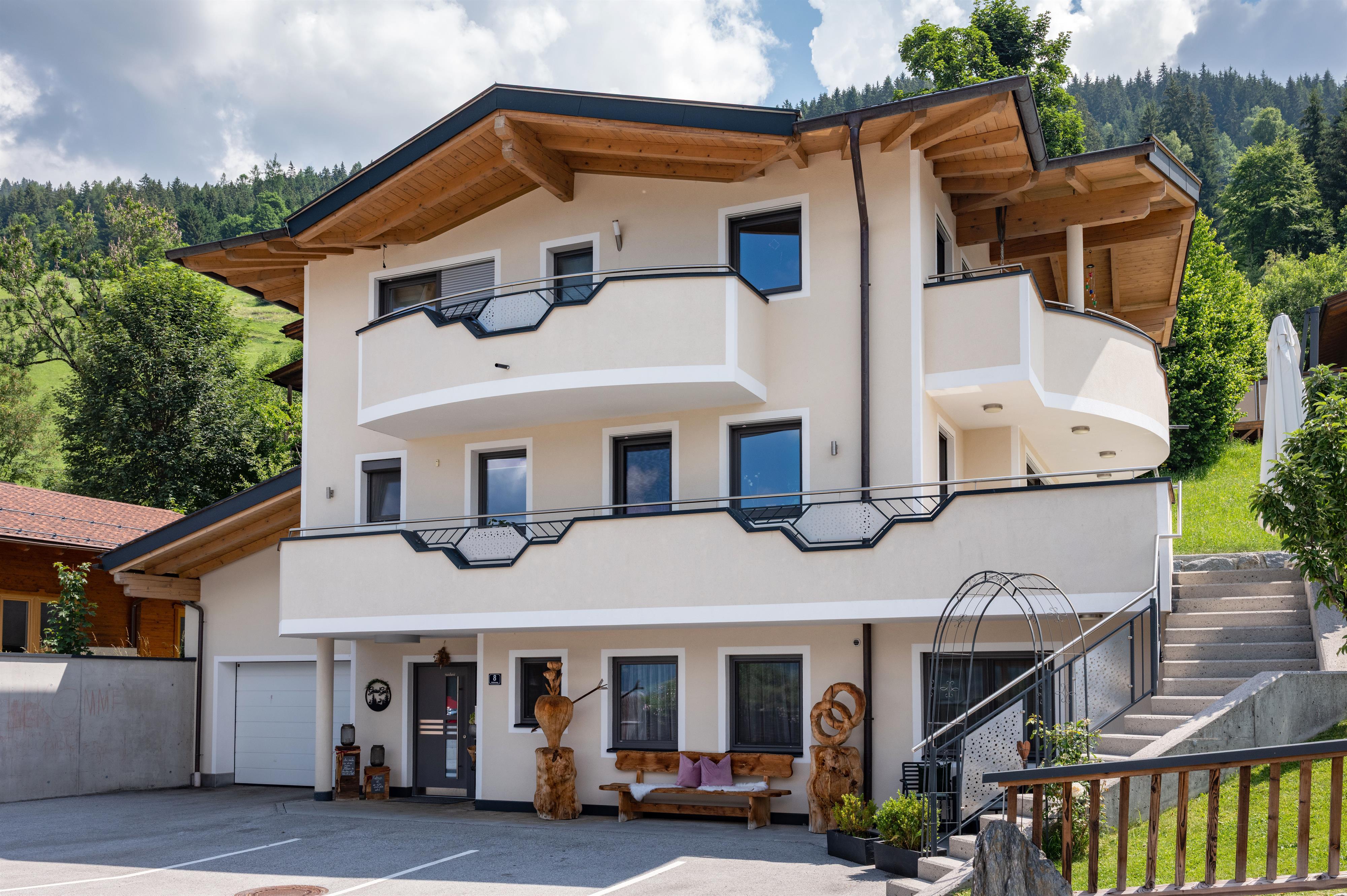 Modernes Mehrfamilienhaus mit weißen Wänden, Balkonen und Holzdetails, umgeben von Natur im Hintergrund.