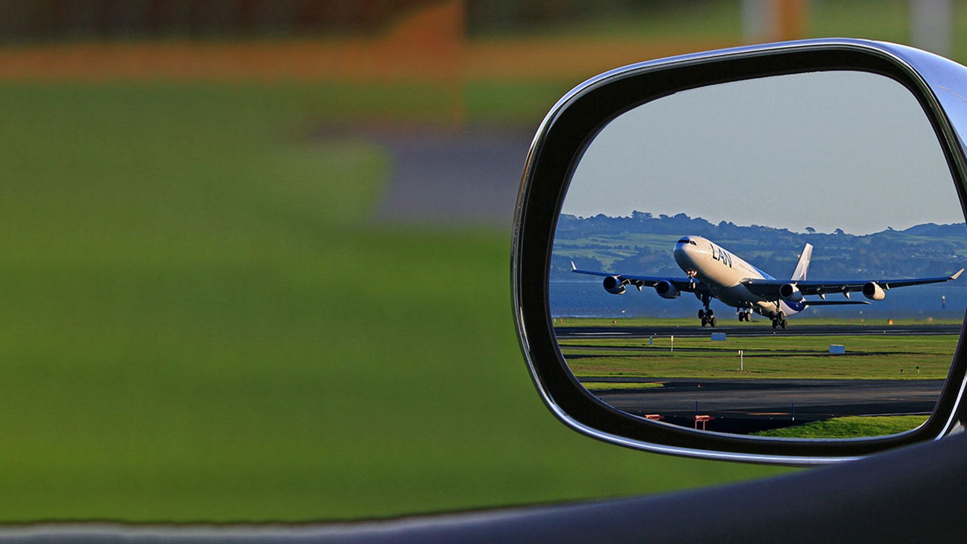 View through a car side mirror of an airplane taking off or landing on a green runway. Symbolic image for air travel to Mayrhofen followed by a car journey.