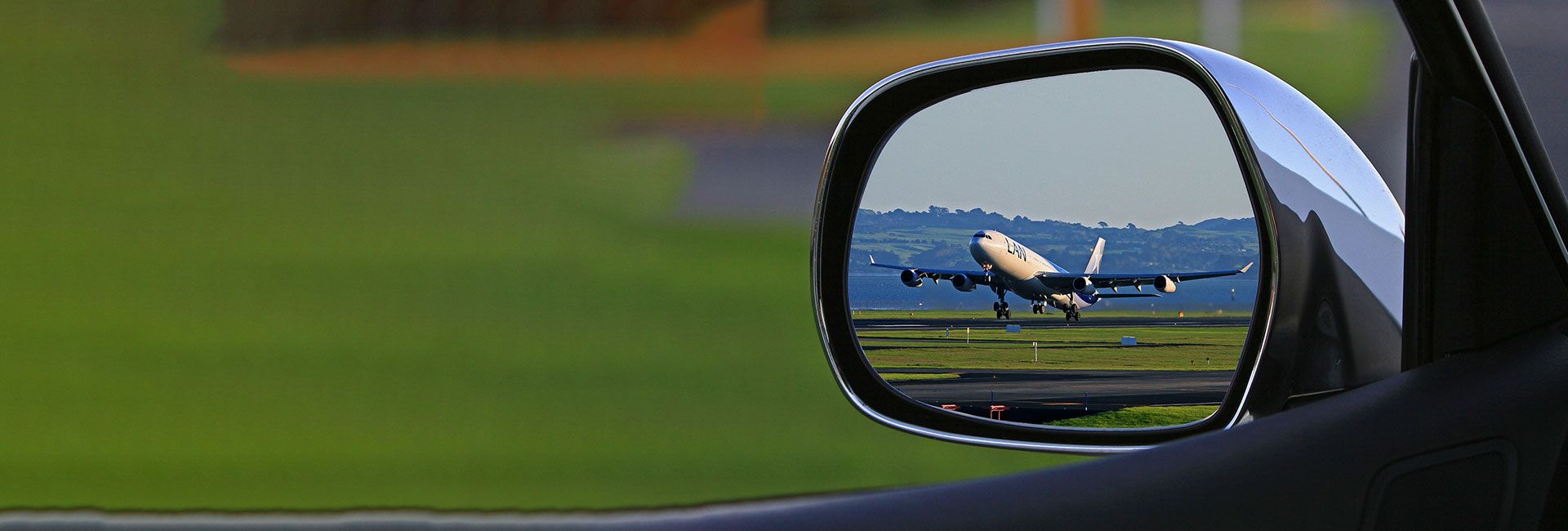 View through a car side mirror of an airplane taking off or landing on a green runway. Symbolic image for air travel to Mayrhofen followed by a car journey.