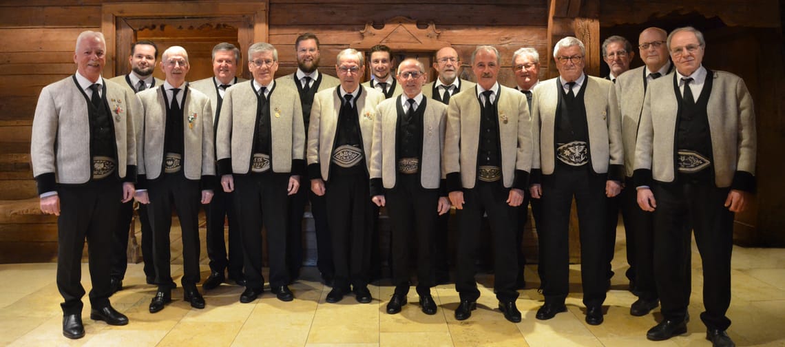 Im Bild ist der Männergesangsverein Mayrhofen abgebildet. Die Männer tragen die Zillertaler Sonntagstracht mit schwarzer Hose, schwarzen Schuhen, weißes Hemd mit schwarzen Gilet und Krawatte sowie die traditionelle graue Tuxer Jacke und einen Ranzen.