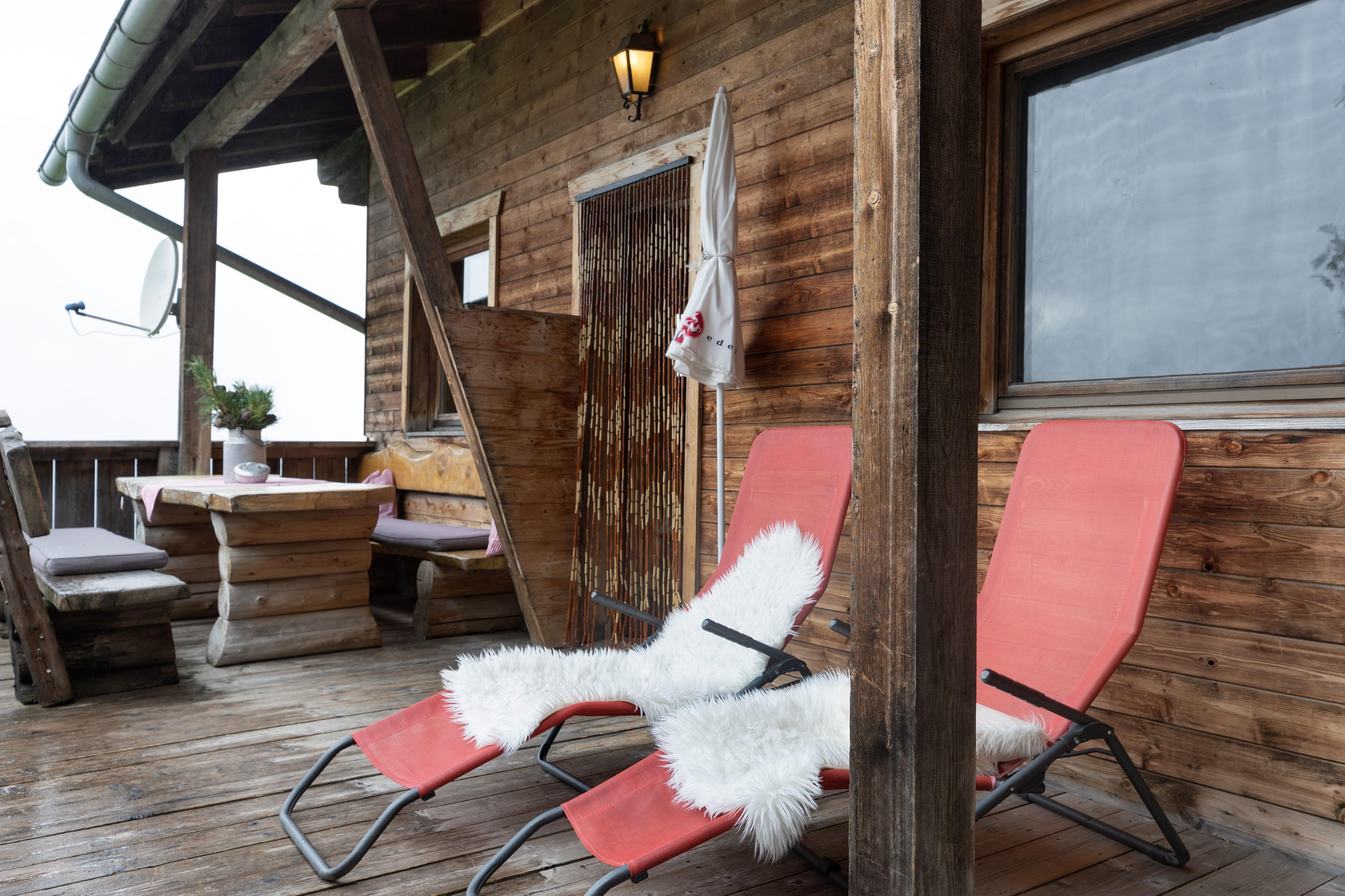 Balkon mit roten Liegestühlen, weißen Kissen, Holzverkleidung und Blick nach draußen bei bewölktem Himmel.