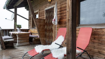 Balkon mit roten Liegestühlen, weißen Kissen, Holzverkleidung und Blick nach draußen bei bewölktem Himmel.