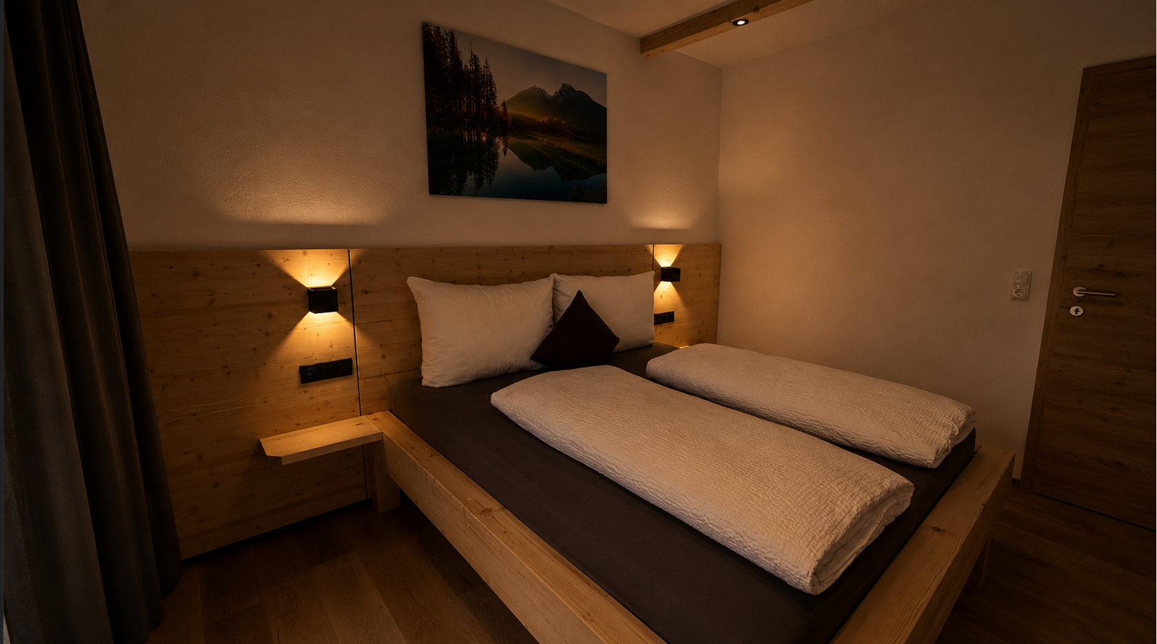 Ein gemütliches Schlafzimmer mit Doppelbett, Holzkopfteil, Wandlampen und Bergbild an der Wand.