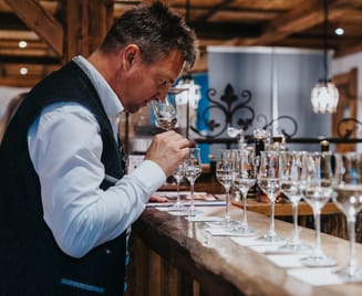 Ein Brennmeister riecht konzentriert an einem Glas Edelbrand. Auf der Theke vor ihm stehen mehrere Gläser zur Verkostung bereit.