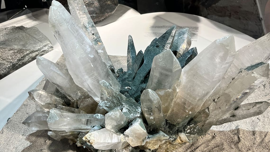 Close-up of an impressive rock crystal formation in the "Hidden Treasures" exhibition at the Ginzling Nature Park House. The clear and shimmering crystals emerge from a rocky base.