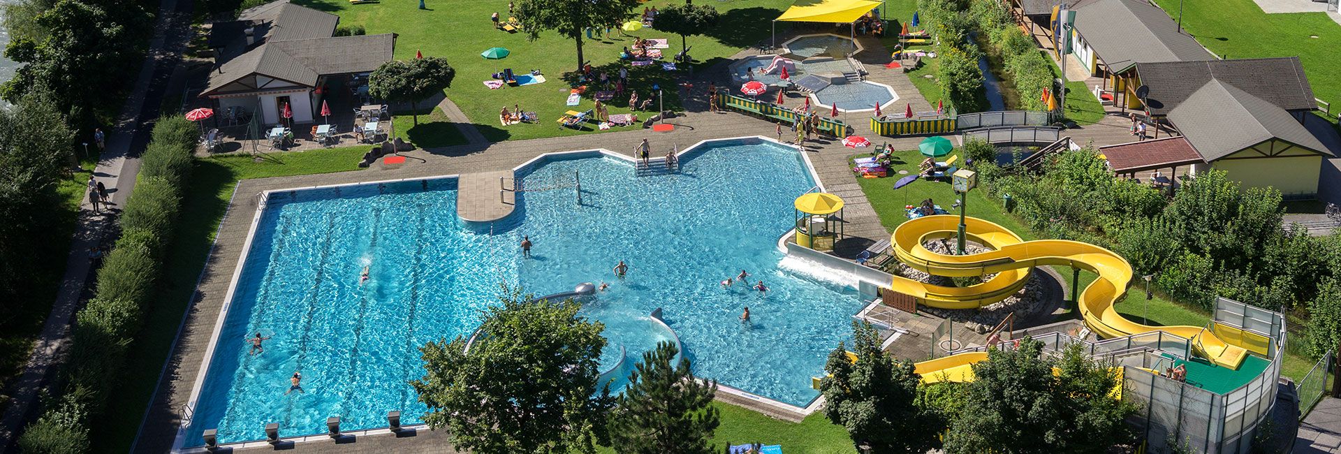 Aerial view of the outdoor pool at Summerworld Hippach in Zillertal with leisure pool, sports pool, slides, kids’ area, and large sunbathing lawns – perfect for families and swimmers.