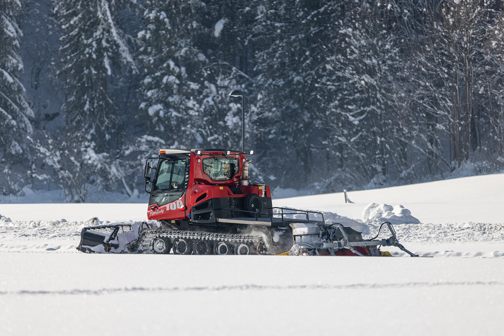 A red snow groomer preparing the cross-country trail in Mayrhofen-Hippach, surrounded by snowy fields and a winter forest