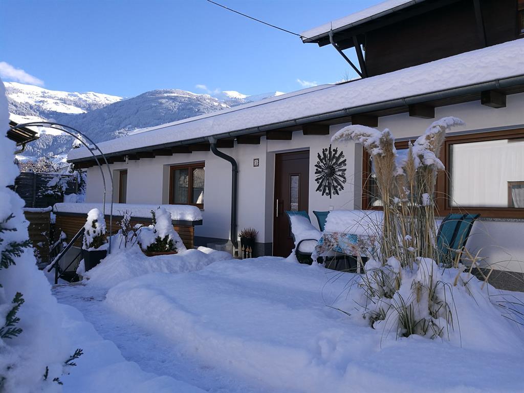 Ein Schneegestütztes Haus mit Terrasse, umgeben von verschneiten Bergen im Hintergrund.