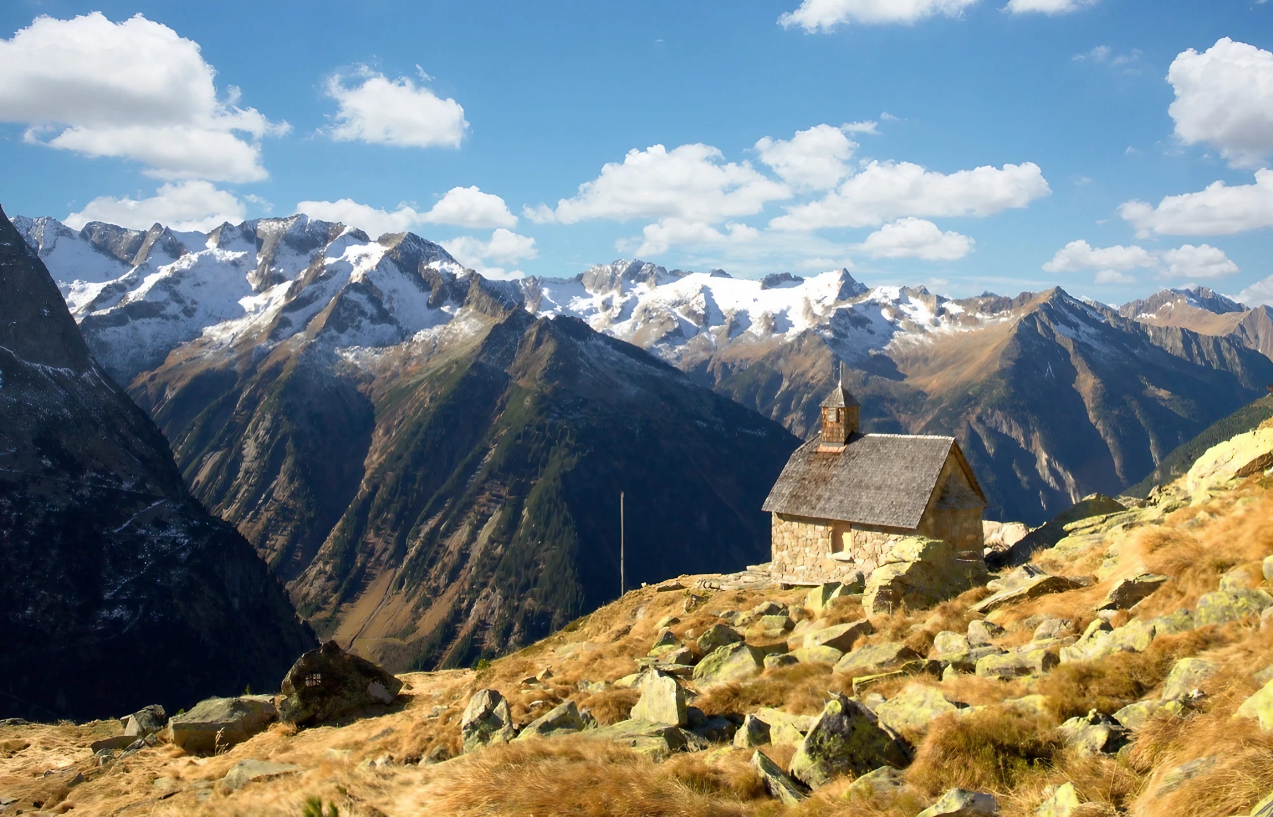 Kleine Kapelle am Berg umgeben von Steinen und Berge im Hintergrund