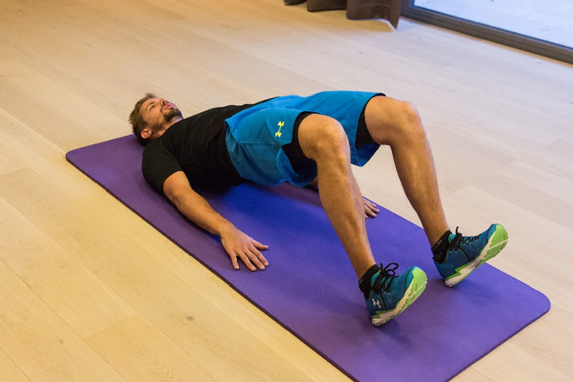 Pelvic lifts - Chris Ebenbichler Man performing glute bridge exercise on yoga mat in training room in Mayrhofen. Christoph Ebenbichler demonstrates ski fitness training for back, glutes and core stability – get fit for winter.