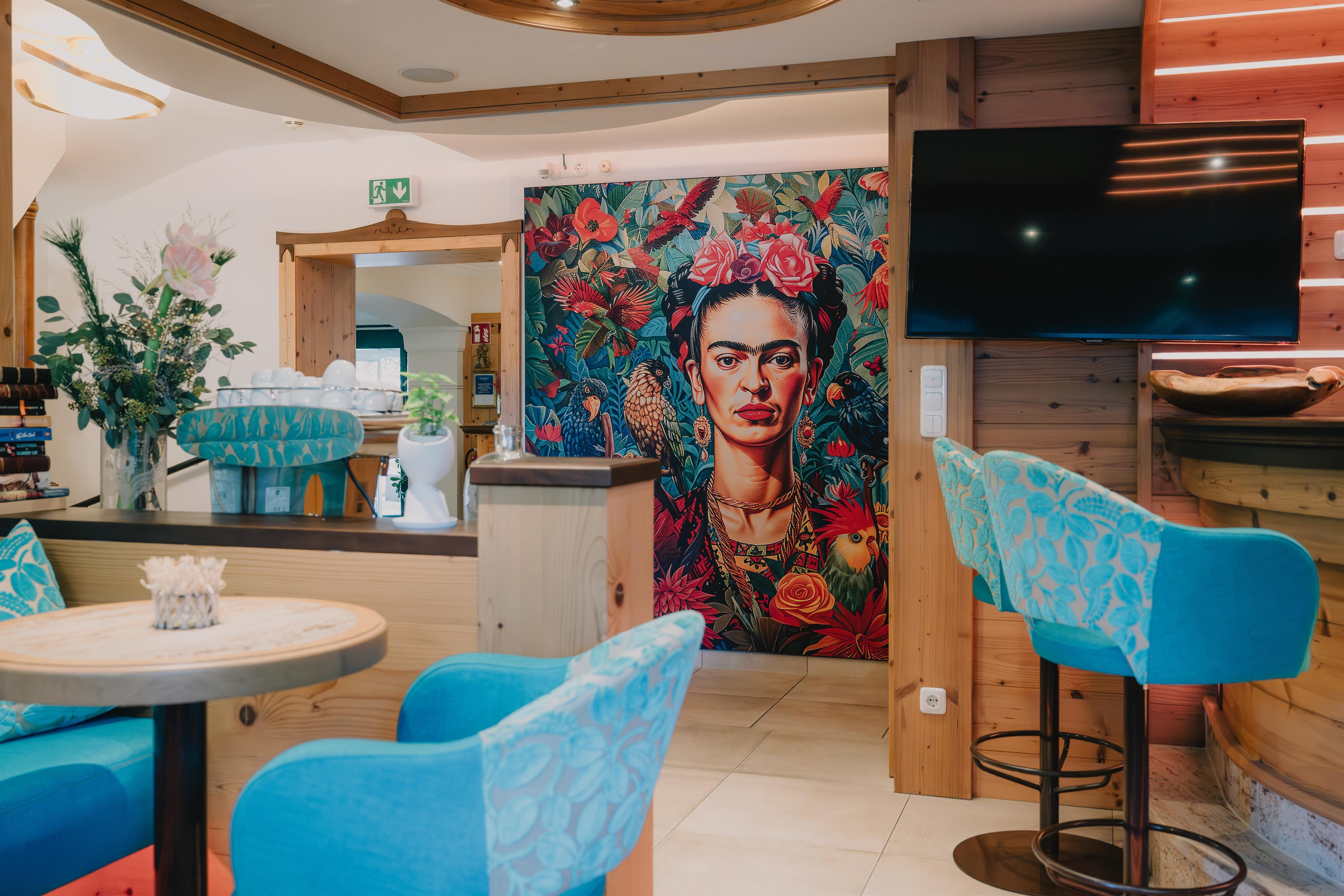 View of a colorful Frida Kahlo mural in a cozy café with blue chairs.