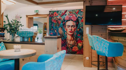 View of a colorful Frida Kahlo mural in a cozy café with blue chairs.