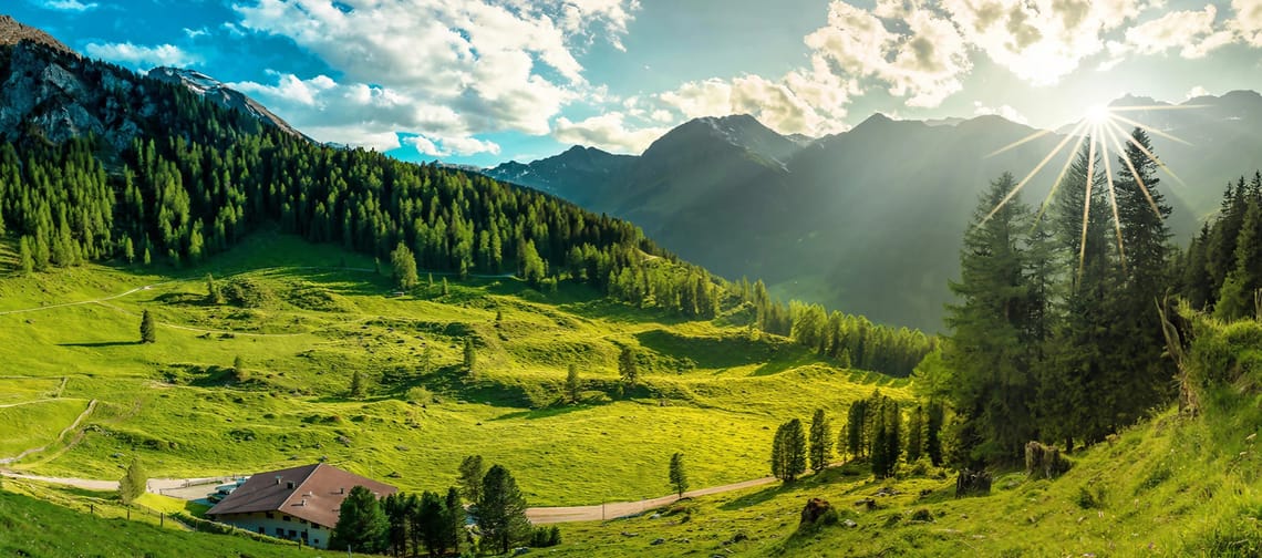 Es zeigt die Löschbödenalm im Tuxer Tal von oben fotografiert, man sieht die Alm, viele Bäume und die Sonne scheint hinter den Wolken hervor