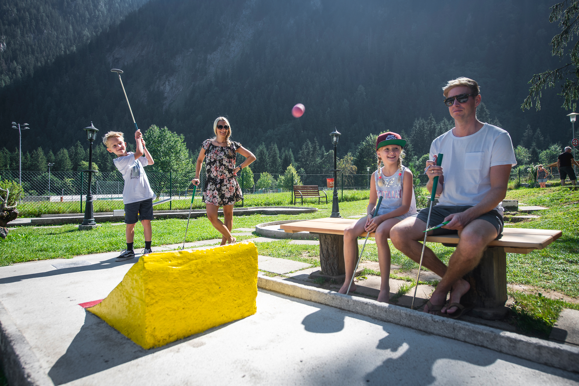 Eine Familie spielt Minigolf, im Hintergrund ist Wald zu sehen