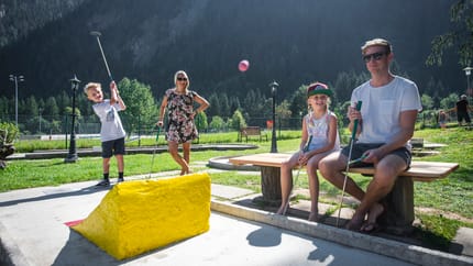 Eine Familie spielt Minigolf, im Hintergrund ist Wald zu sehen