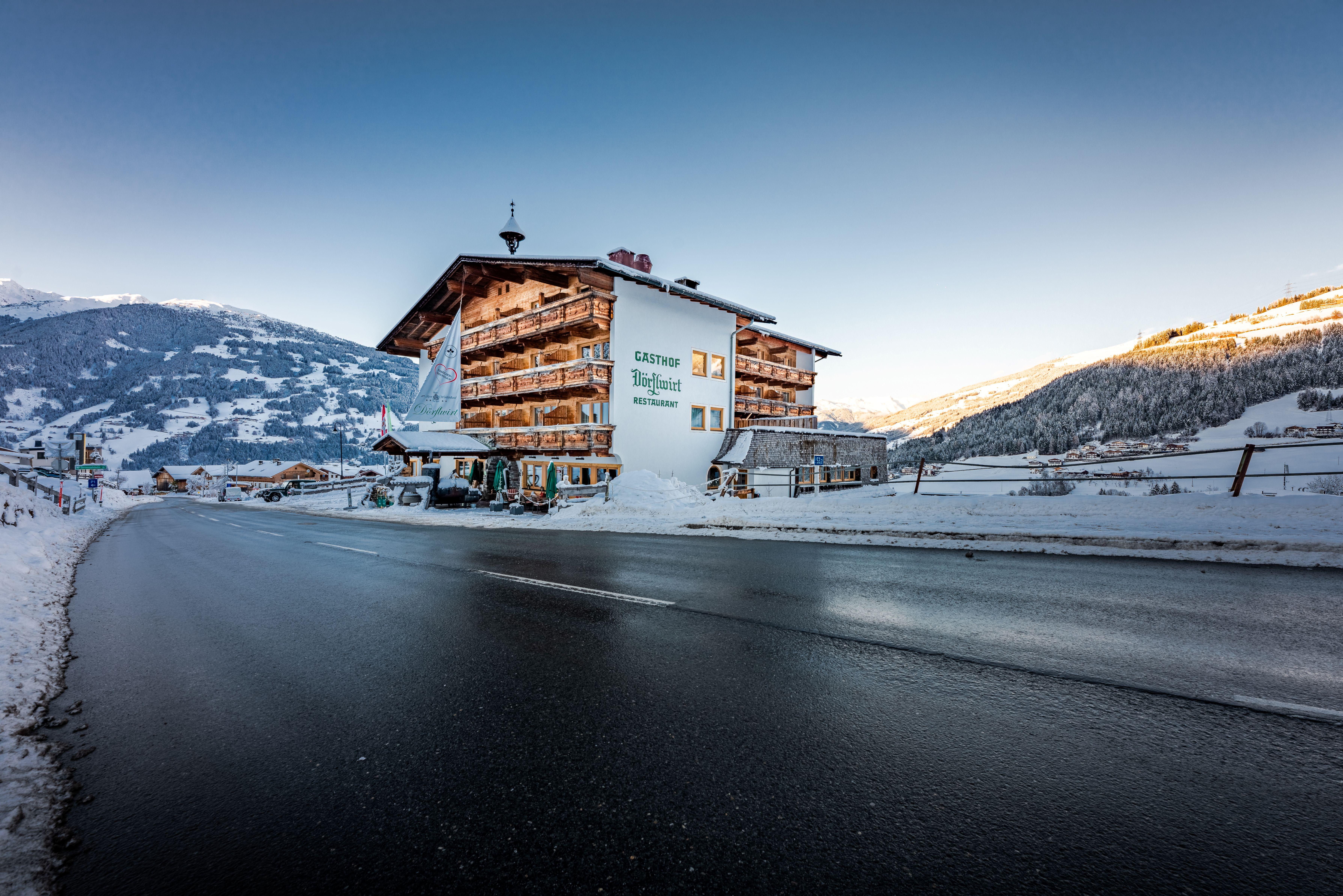 A snowy mountain village with a guesthouse, surrounded by snow-covered mountains and clear sky.