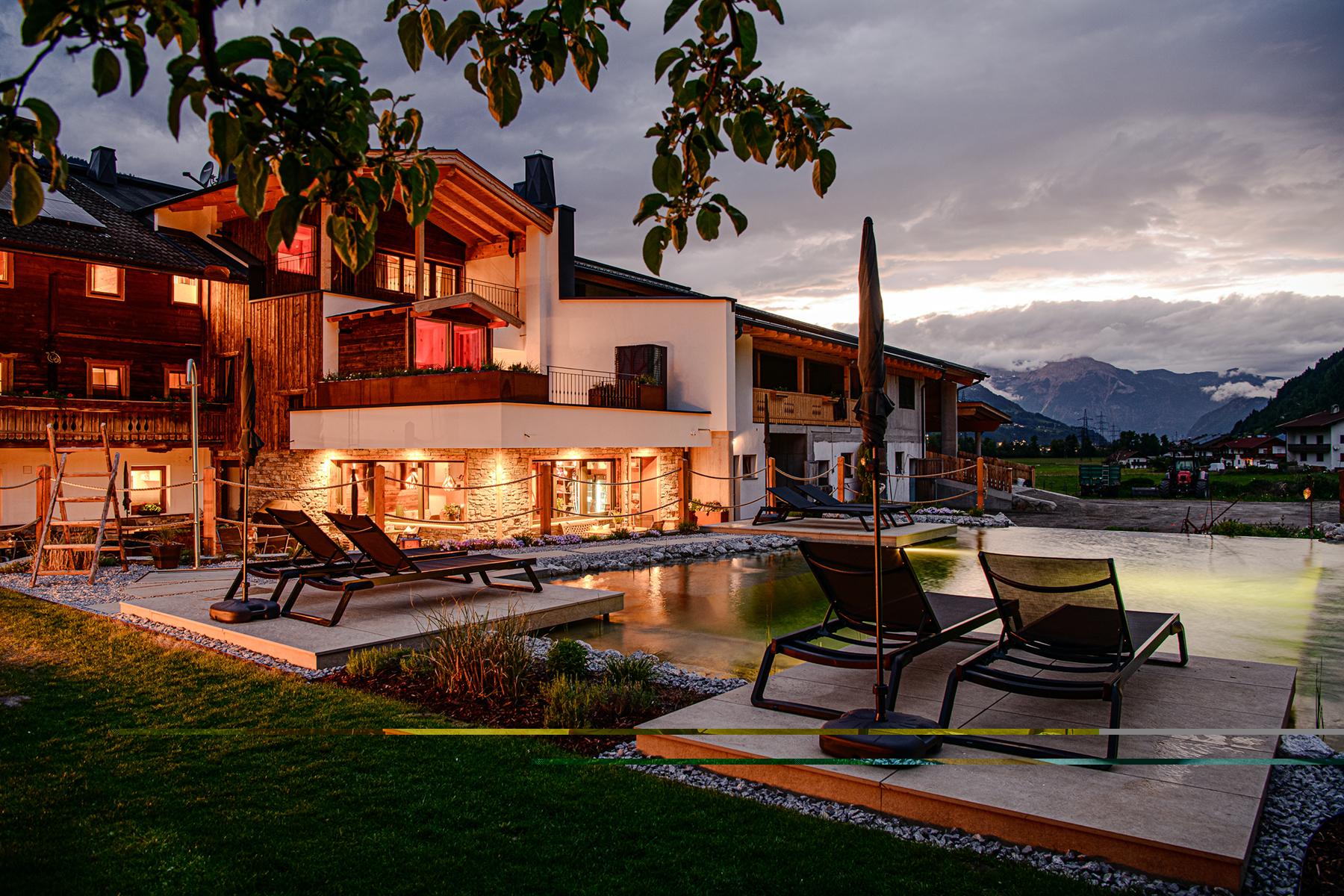A modern house with a terrace, lounge chairs, and pool at sunset in the mountains.