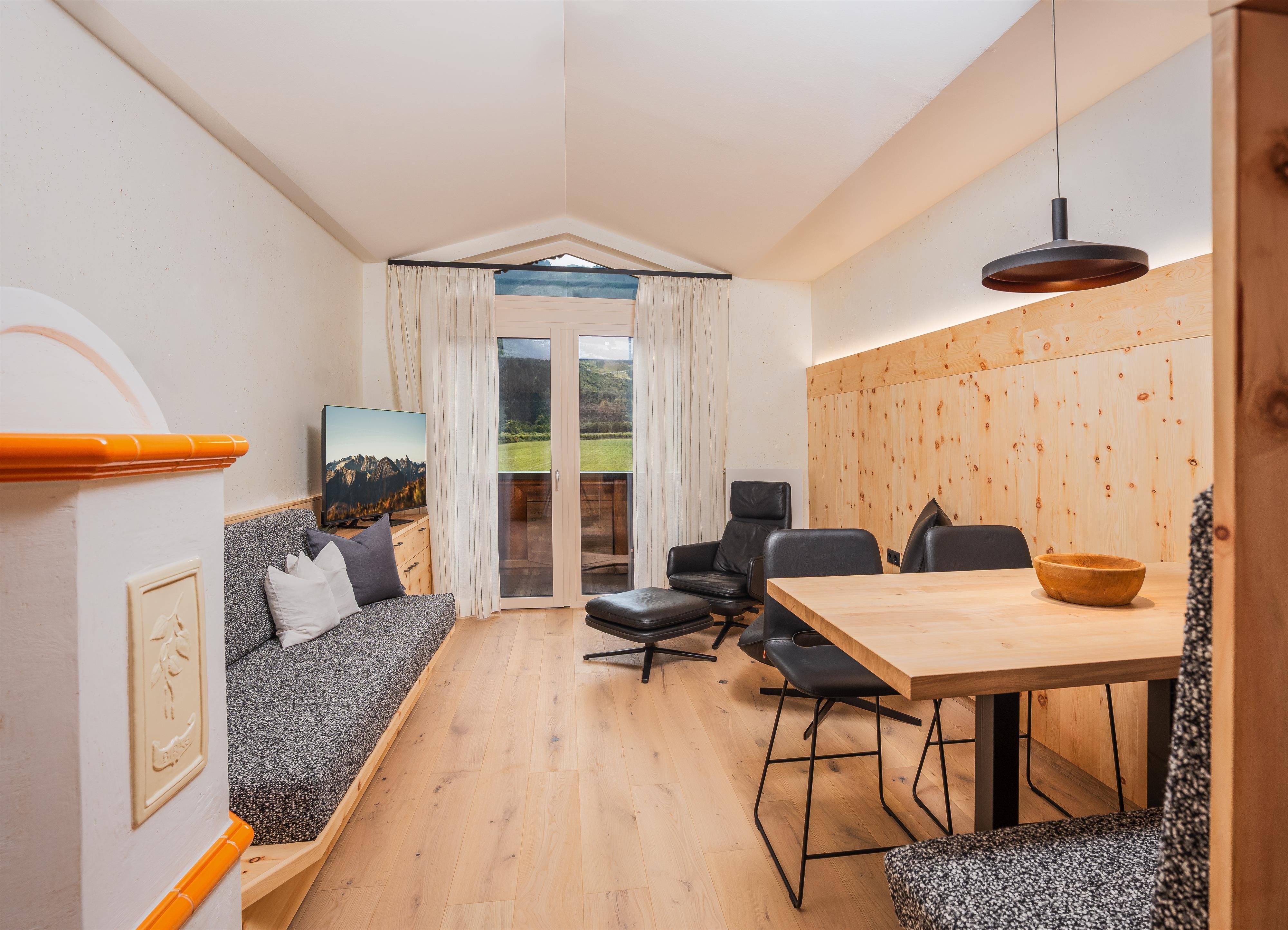 Gemütliches Wohnzimmer mit Sofa, Fernseher, großen Fenstern und Holzwand, helle, einladende Atmosphäre.