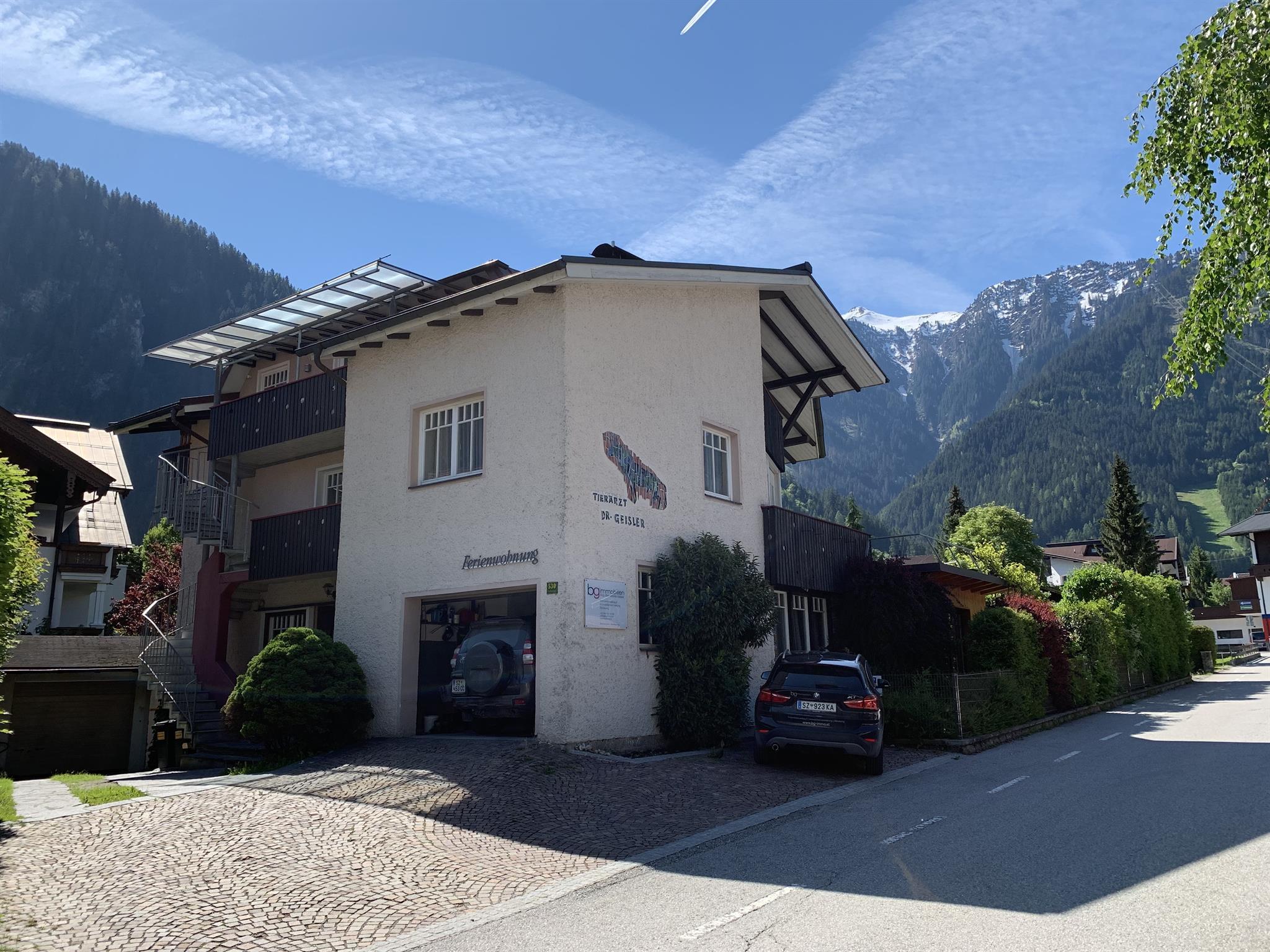 Buildings in a mountain village with snow-capped peaks, blue sky, and clouds, in a peaceful rural setting.