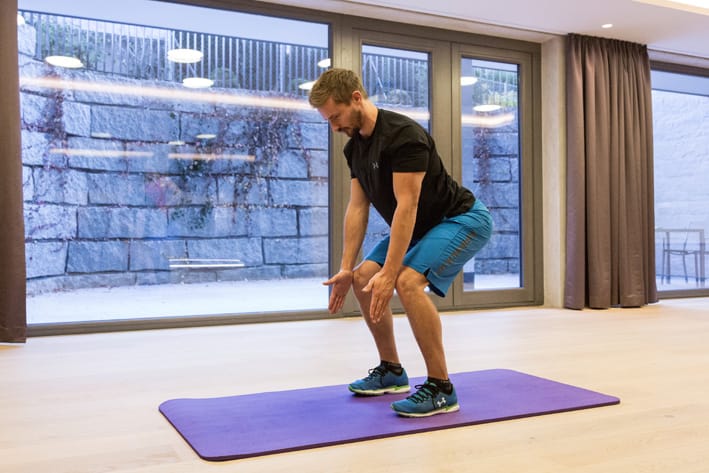 Standing Extensions - Chris Ebenbichler Man performing standing extensions exercise on yoga mat in training hall in Mayrhofen. Christoph Ebenbichler demonstrates a functional back and leg workout for ski fitness – get fit for winter.