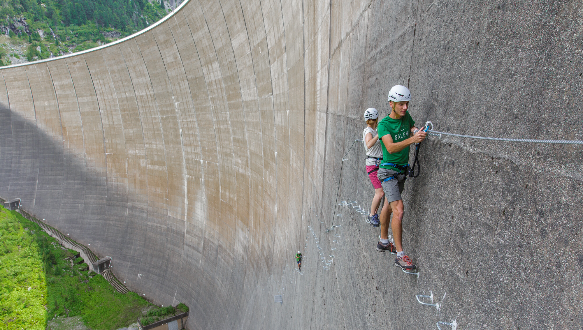 Klettern an der Schlegeis Staumauer im Zillertal: Kletterer im Klettersteig Schlegeis 131 an der hohen Betonwand, gesichert mit Kletterausrüstung und umgeben von alpiner Landschaft.
