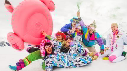 Personen in bunter Kleidung mit einer Flamingo Luftmatratze am Berg im Schnee