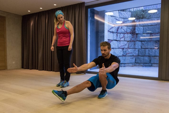 Man performing single-leg squat (pistol squat) in training room in Mayrhofen, watched by trainer. Christoph Ebenbichler demonstrates balance, strength and stability exercise for ski fitness.