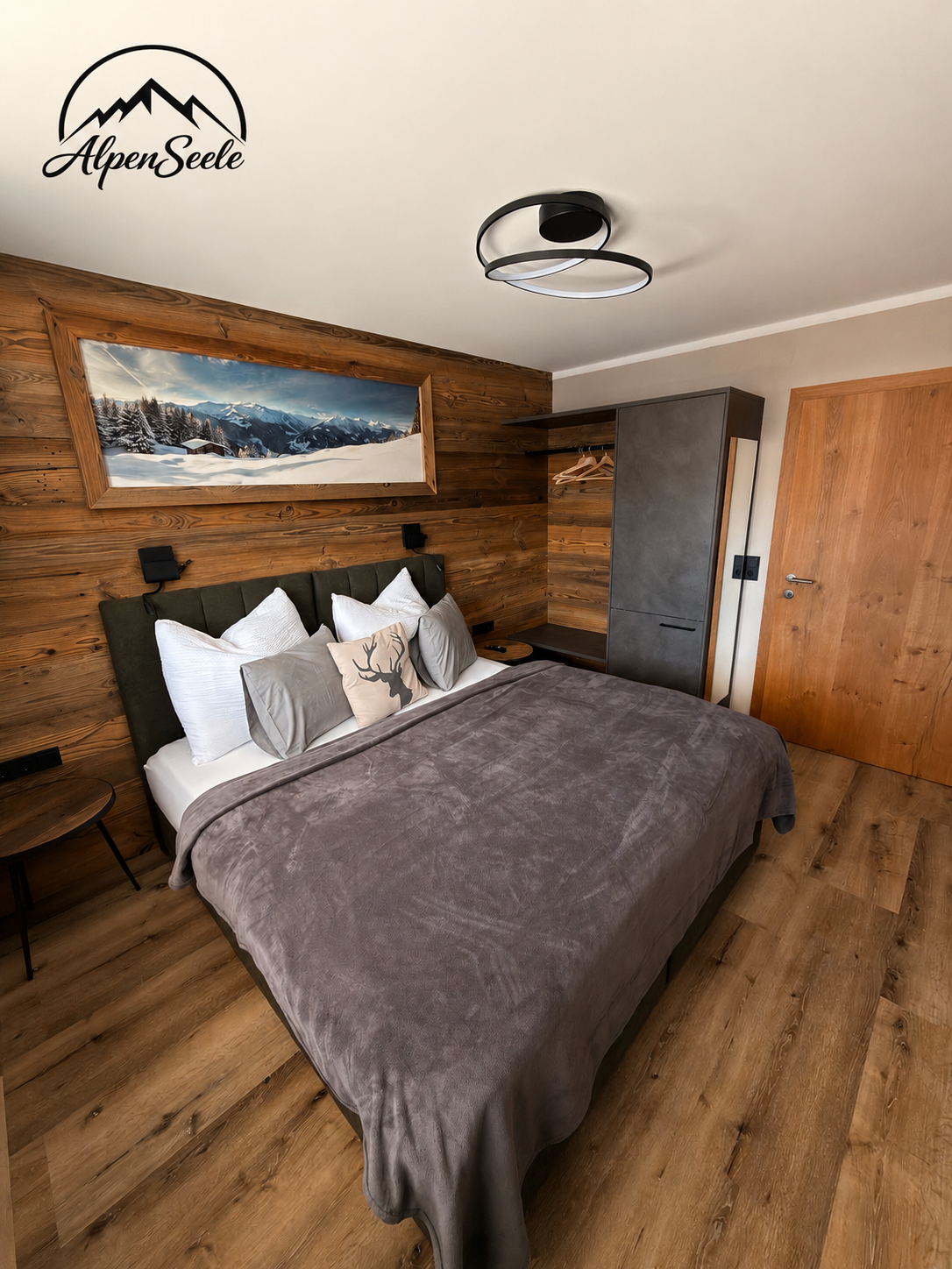 Schlafzimmer mit Holz-Wand, Bett mit grauem Bezug, Wandbild der Berge, moderne Deckenleuchte, Holz-Tür.