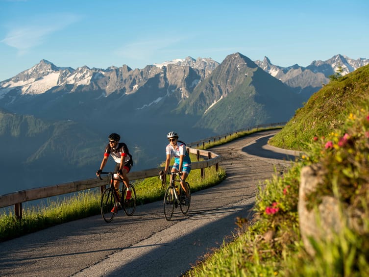 Zwei Rennradfahrer auf der Zillertaler Höhenstraße mit Alpenpanorama im Hintergrund bei Sonnenschein – Sommer, Sport und Natur in den Tiroler Bergen.