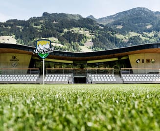 Lindenstadion football stadium in Hippach featuring modern timber architecture, seating stands, and a view of the green Alpine landscape; home ground of SK Hippach in Tyrol.
