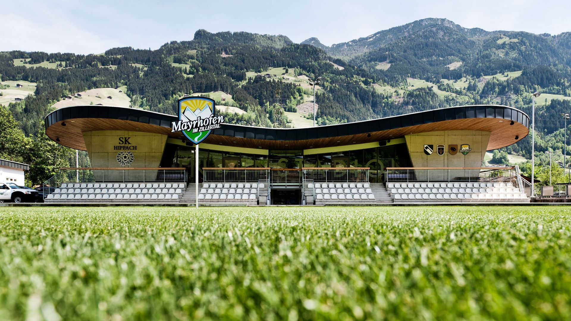 Fußballstadion Lindenstadion in Hippach mit moderner Holzarchitektur, Sitztribüne und Blick auf grüne Alpenlandschaft, Sportanlage des SK Hippach in Tirol.