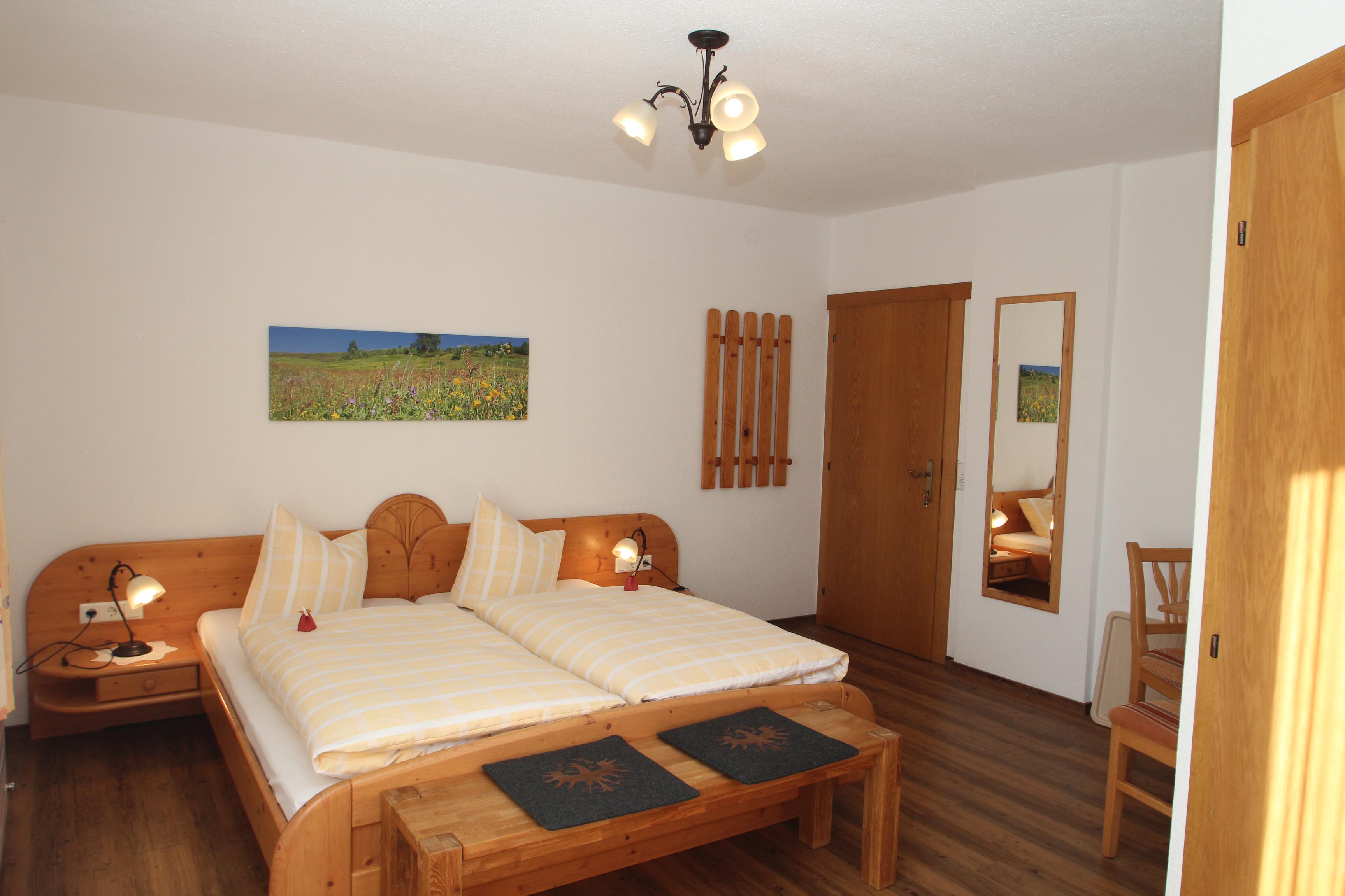 Bedroom with two beds, wall art, wooden furniture, mirror, bright and cozy setting.