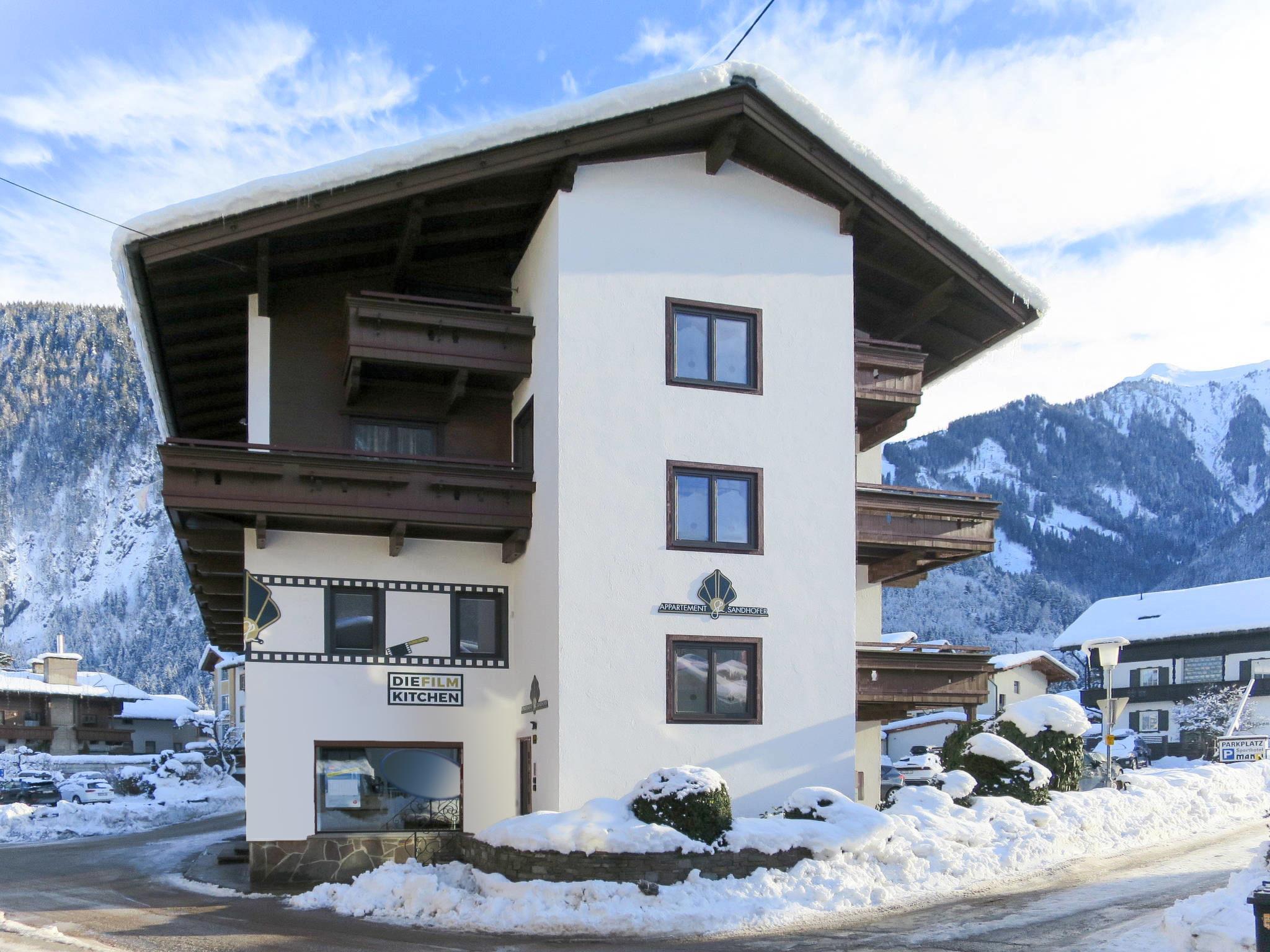Mehrstöckiges Ferienhaus in Schneelandschaft mit Bergen im Hintergrund, Beschilderung für Küche und Film im Erdgeschoss.