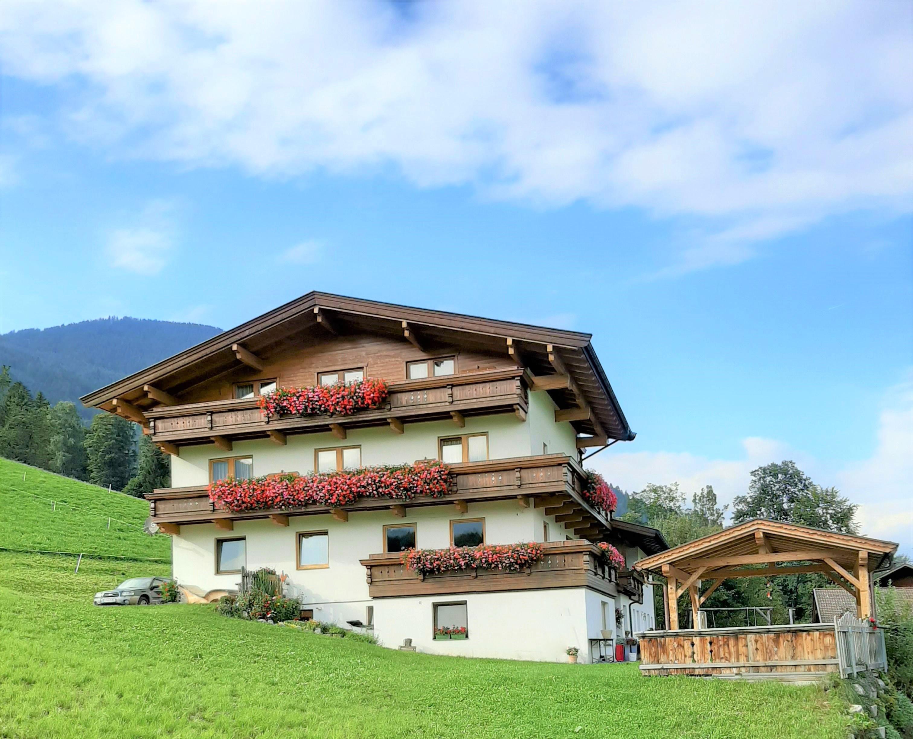 Multi-story house with balcony and red flowers, green lawn, and mountains in the background.