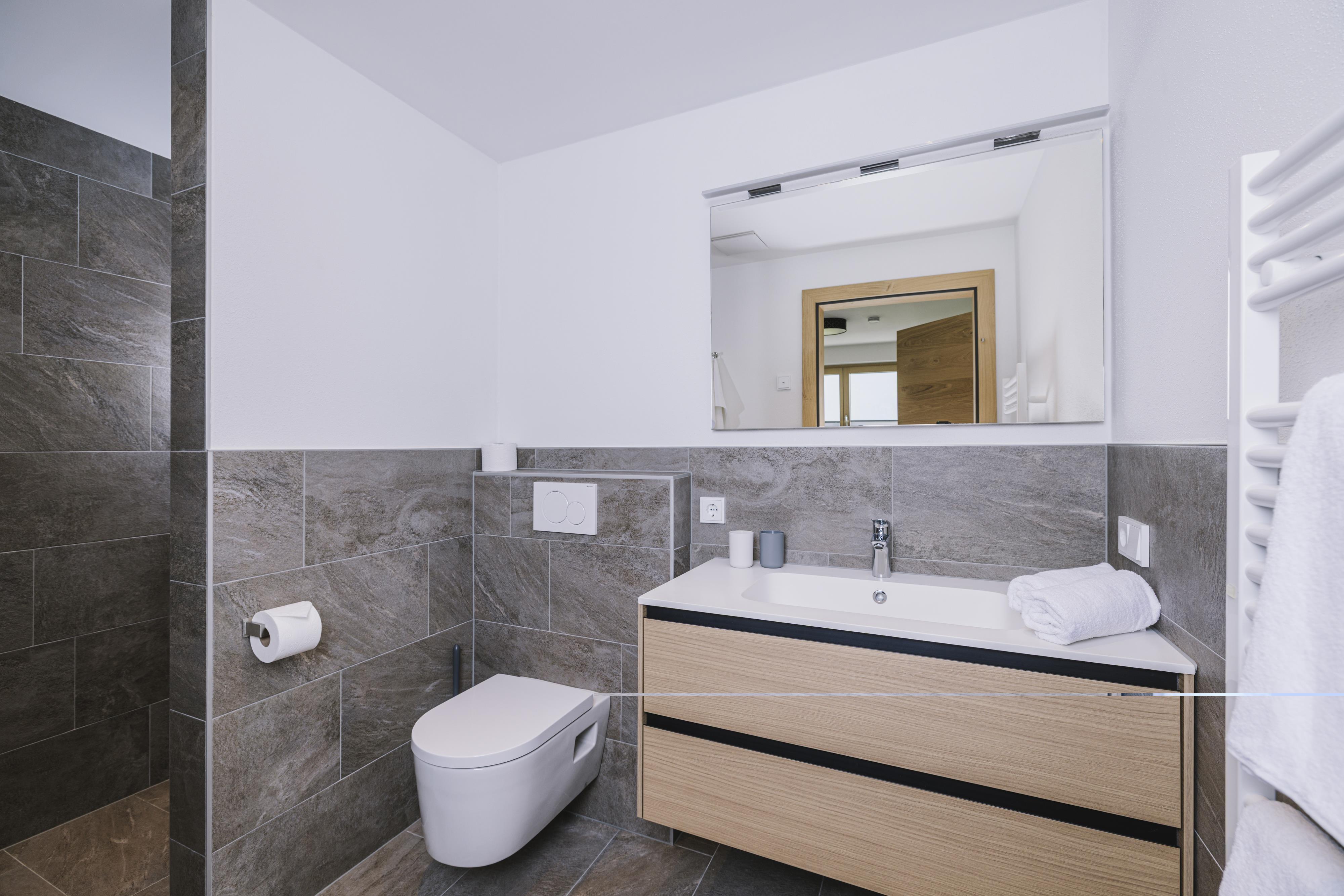 Modern bathroom with mirror, sink, toilet, and towel radiator in neutral tones.