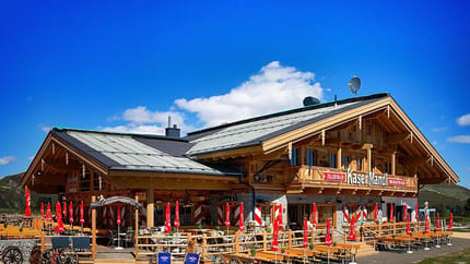 Im Bild sieht man die Almhütte Kasermandl mit einer großen Terrasse. Im Hintergrund blauer Himmel.