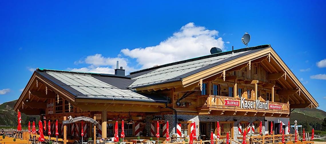 Im Bild sieht man die Almhütte Kasermandl mit einer großen Terrasse. Im Hintergrund blauer Himmel.