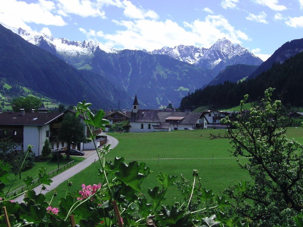 Scenic view of green fields, houses, a church, and snow-capped mountains in the background.