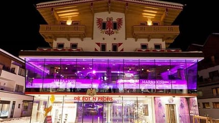 The image shows the Harakiri Bar from the outside at night. Pink LED lights shine from the second floor, giving the building a modern and striking appearance.