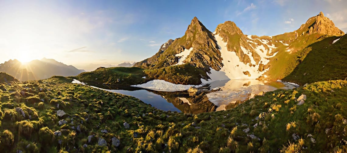 Sonnenaufgang beim Eiskarsee, man sieht einen schneebedeckten Berg und Gras umliegend