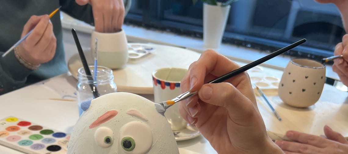 A ceramic piece that looks like a monster is being painted by a person holding a brush.