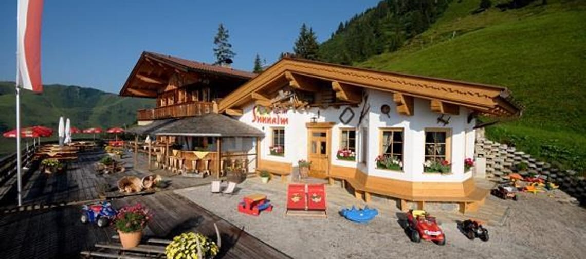 The image shows the Schiestl's Sunnalm in summer, with a terrace and a small playground.