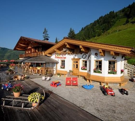 The image shows the Schiestl's Sunnalm in summer, with a terrace and a small playground.
