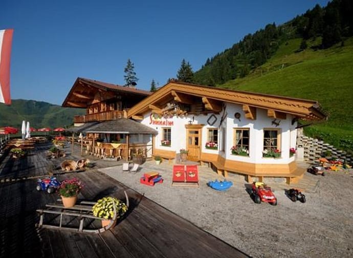 The image shows the Schiestl's Sunnalm in summer, with a terrace and a small playground.