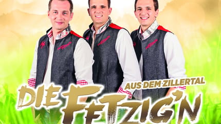 Drei junge Männer in Trachtenjacken vor buntem, fröhlichem Hintergrund, lächelnd für ein Gruppenfoto.