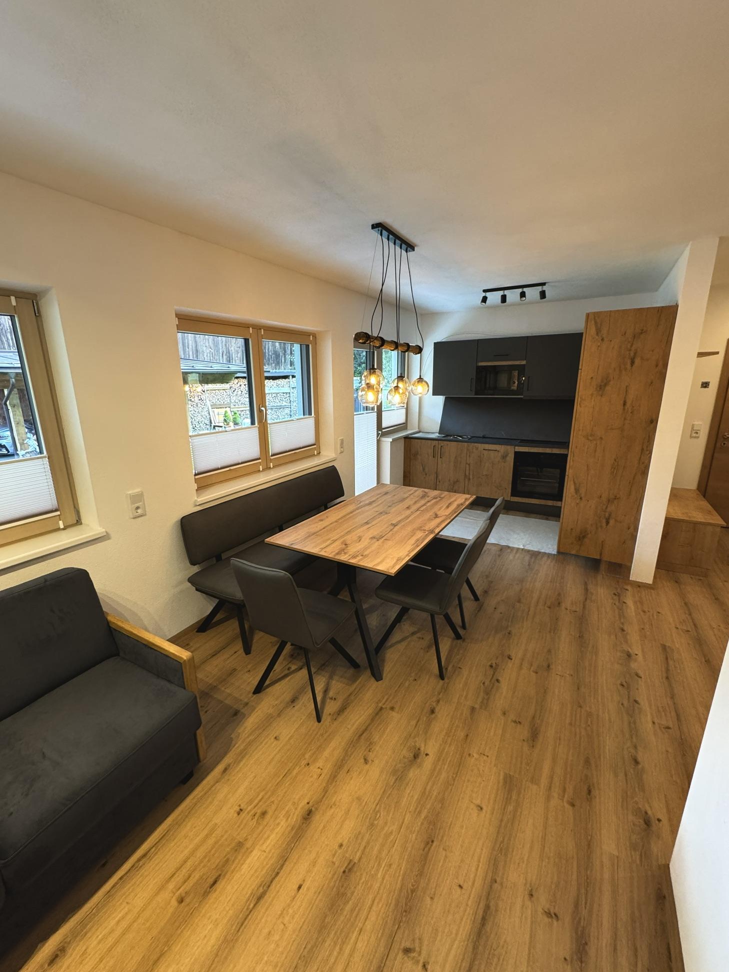 Moderner Essbereich mit Holz-Tisch, schwarzen Stühlen, großen Fenstern und einer modernen Küchenzeile.