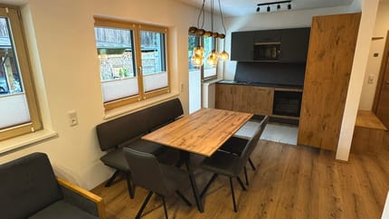 Moderner Essbereich mit Holz-Tisch, schwarzen Stühlen, großen Fenstern und einer modernen Küchenzeile.