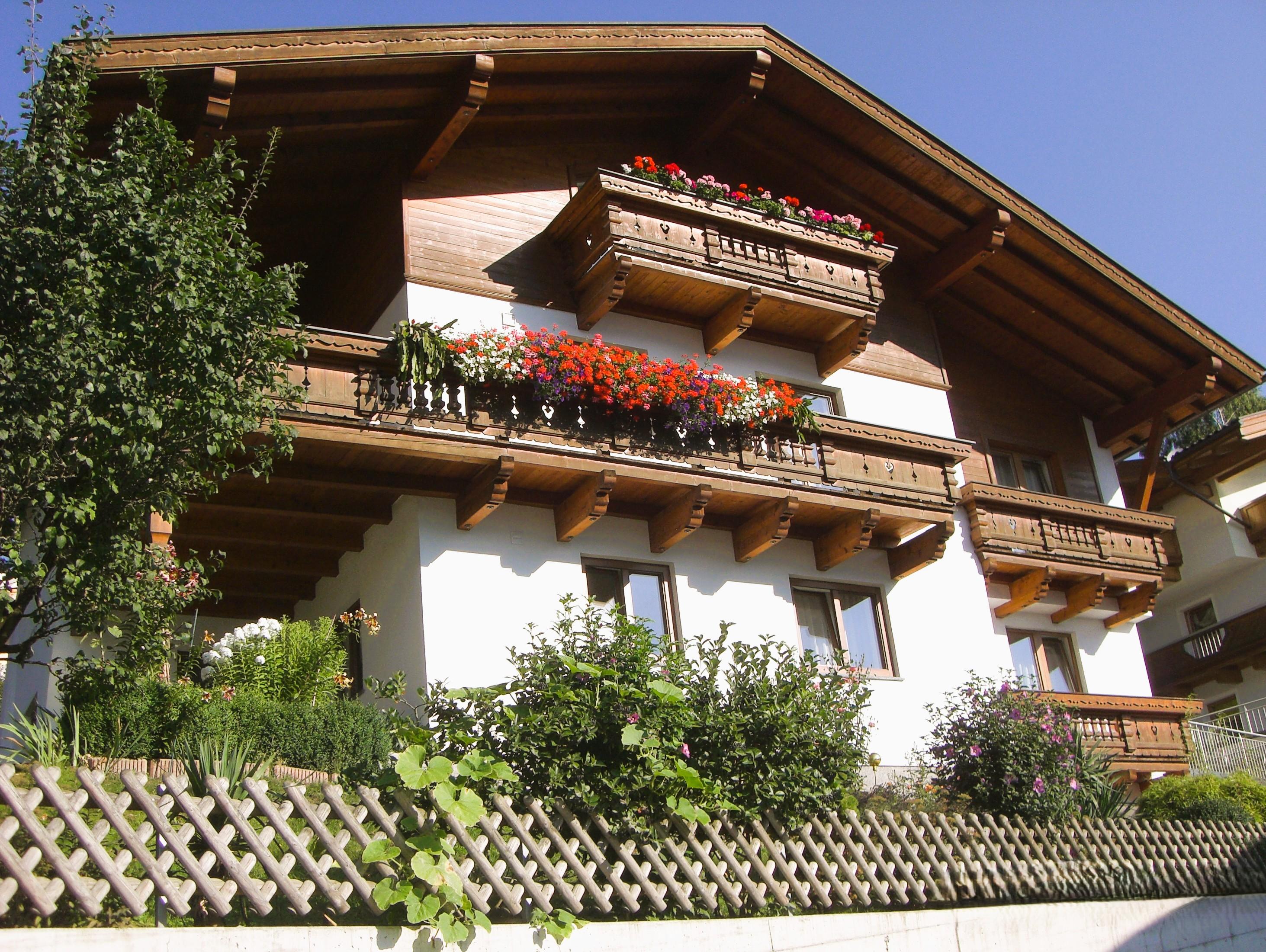 Ein mehrstöckiges Haus mit Holzbalconen und bunten Blumen vor einem blauen Himmel.