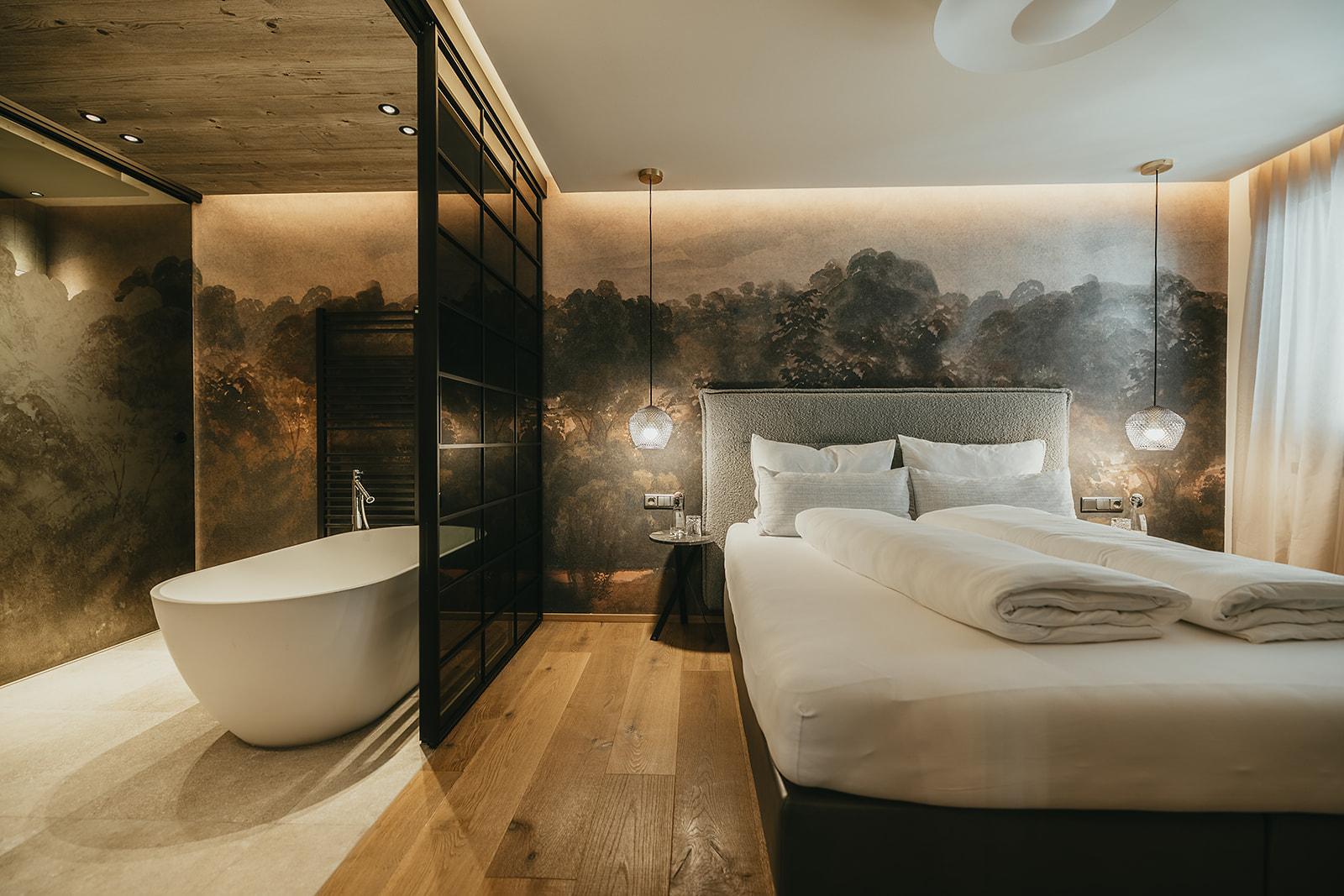 Modernes Schlafzimmer mit Wandbild, Bett, Nachttischen, Hängelampen und freistehender Badewanne im Hintergrund.