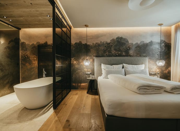 Modernes Schlafzimmer mit Wandbild, Bett, Nachttischen, Hängelampen und freistehender Badewanne im Hintergrund.